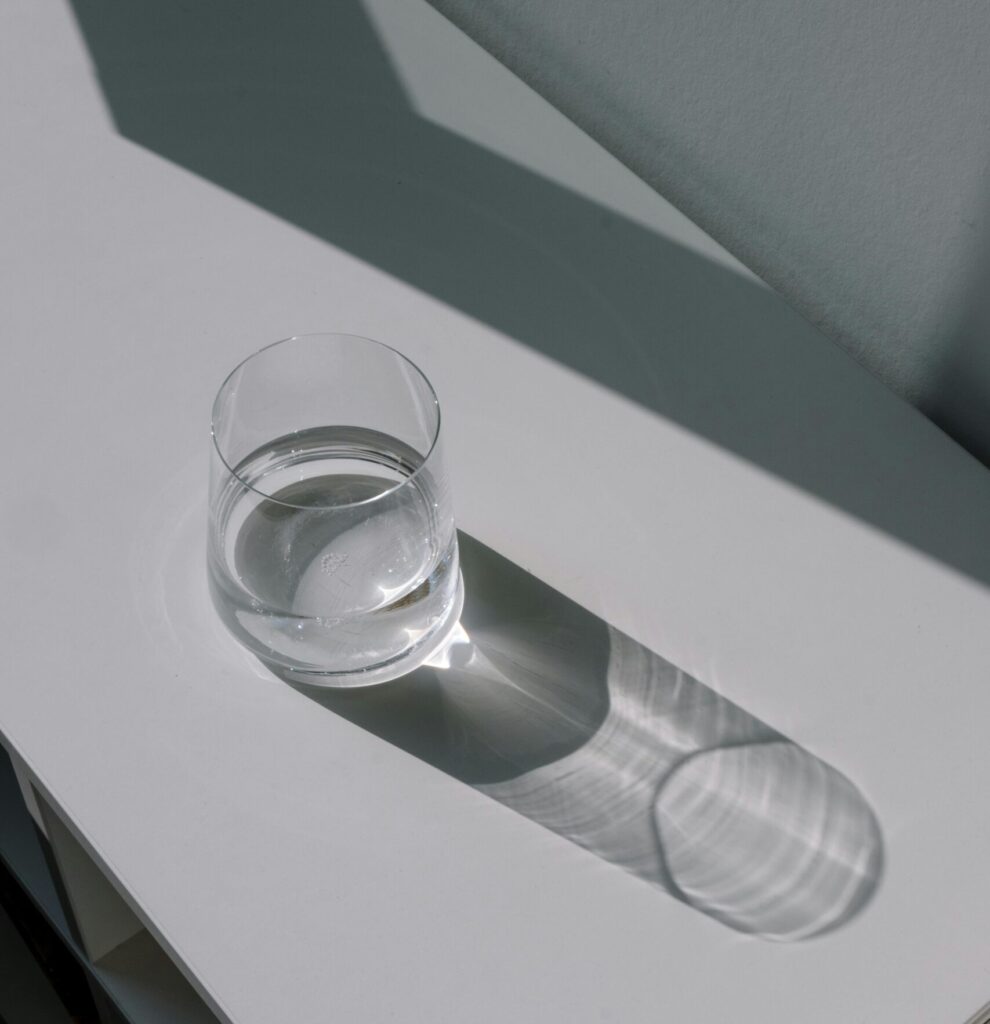 Minimalist photo of a glass of water casting a shadow on a white table.